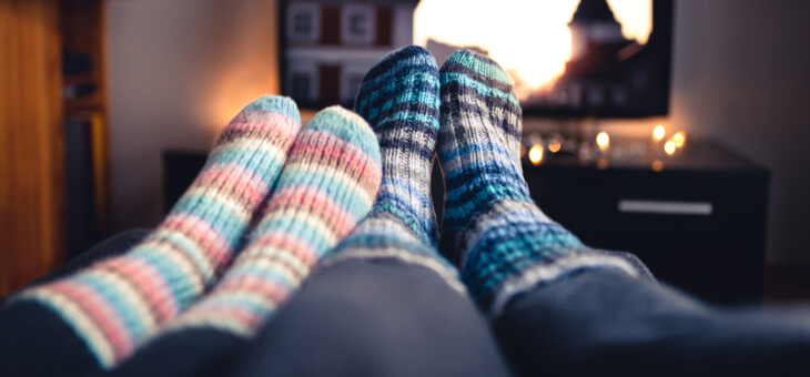 feet of couple relaxing on couch watching tv
