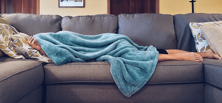 woman lying on couch under blanket