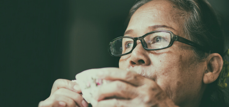 mature woman staring out window while sipping tea