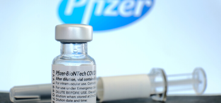 vial of pfizer vaccine and syringe in front of pfizer logo