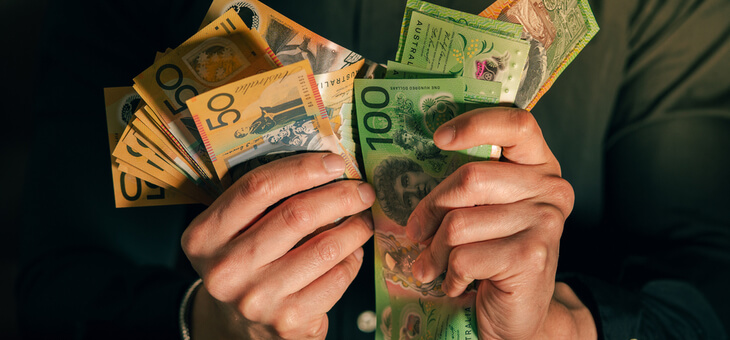 man in suit holding wads of australian fifty and one hundred dollar notes