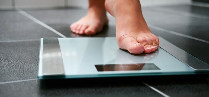 feet of woman stepping on bathroom scales