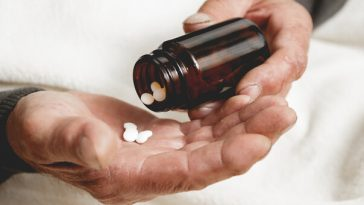 hands older man shaking pills into palm from pill bottle