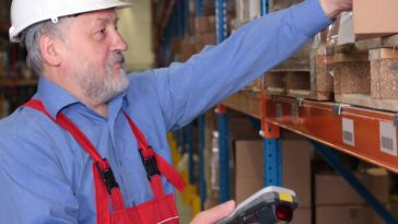 older man in hard hat and overalls working in warehouse