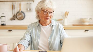 woman sitting at kitchen table paying bills on laptop