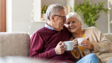 happy retired couple snuggling on couch with coffee