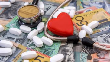 stethoscope, pills and toy heart lying on pile of cash