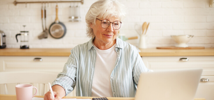 woman sitting at kitchen table paying bills on laptop