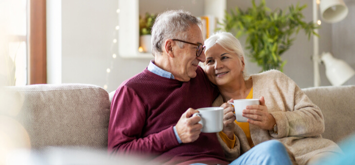 happy retired couple snuggling on couch with coffee
