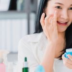woman applying eye cream in front of mirror