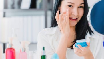 woman applying eye cream in front of mirror