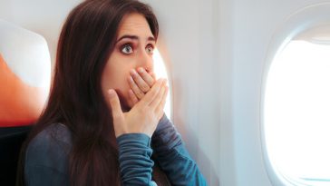 woman sitting on plane with hands over her mouth