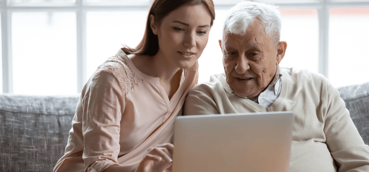 young female carer helping elderly man use computer