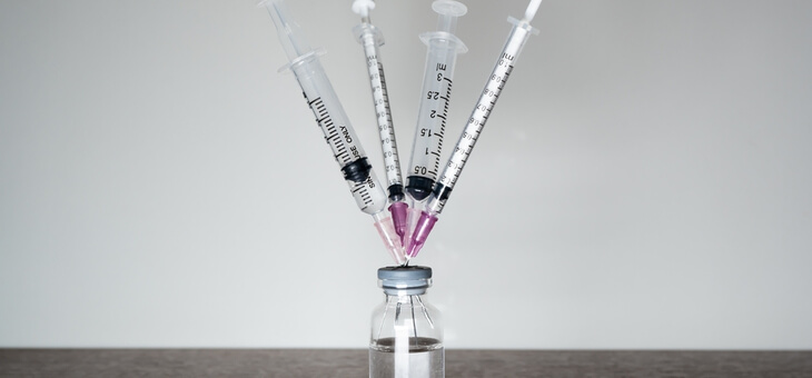 four syringes sticking out of vial of covid vaccine