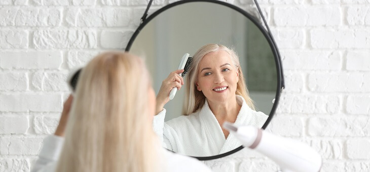 woman brushing and blowdrying hair in mirror