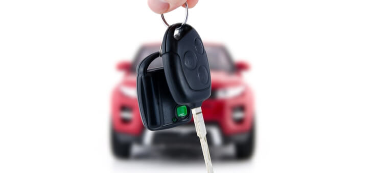 hands holding car keys with new car behind