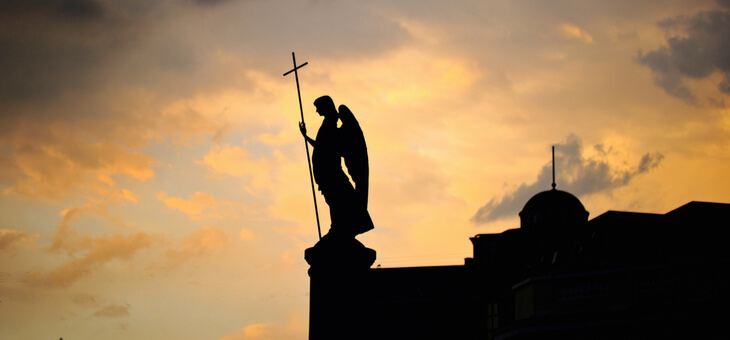 silhouette of angel statue on church top at sunset