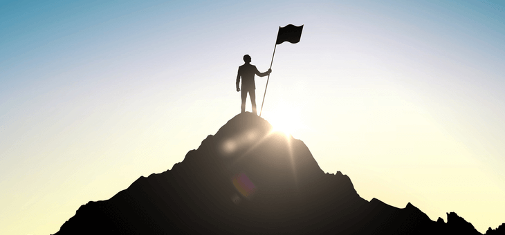 silhouette of man planting flag at top of hill