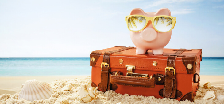 piggy bank wearing sunglasses on suitcase sitting on beach
