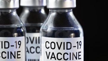 three vials of covid-19 vaccine on black background