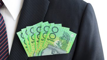 man wearing suit with stack of hundred dollar notes in top pocket