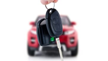 hands holding car keys with new car behind