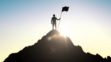 silhouette of man planting flag at top of hill