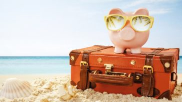 piggy bank wearing sunglasses on suitcase sitting on beach