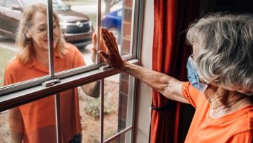 older woman touching her daughter's hand through glass window