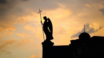 silhouette of angel statue on church top at sunset