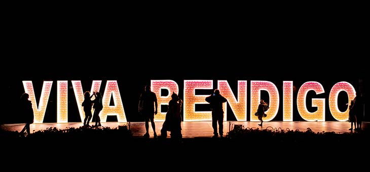 Couples dancing in front of the Viva Bendigo sign by night