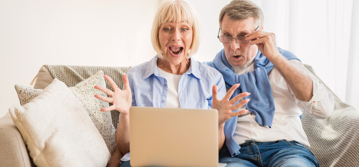excited older couple on couch looking at laptop