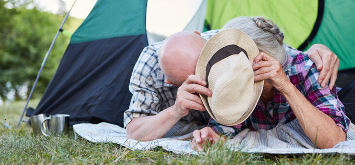 older couple lying in front of tent hiding behind hat
