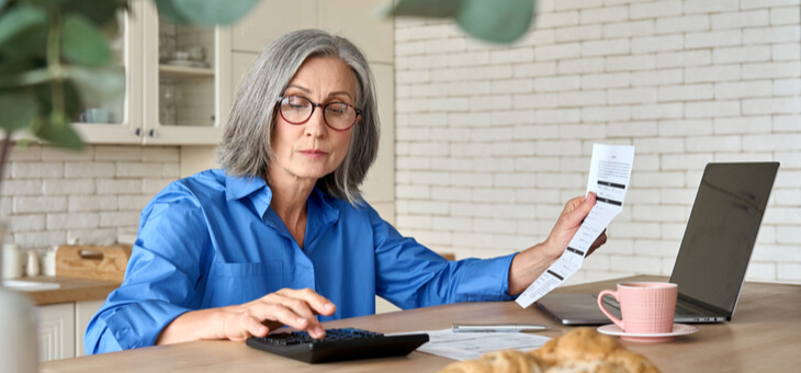 mature woman sitting at kitchen table paying bills on laptop