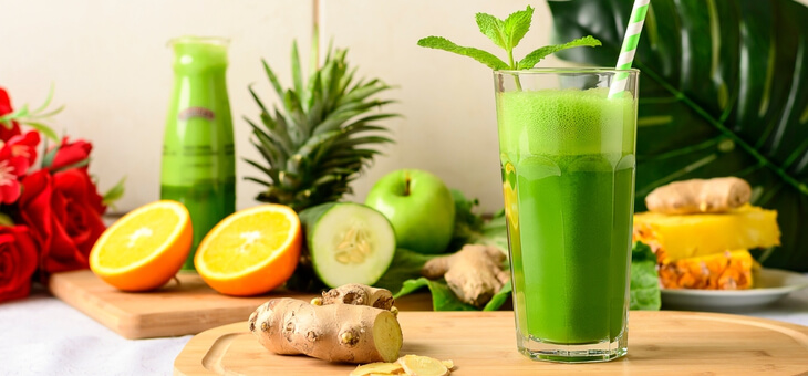 glass of green detox juice surrounded by vegetables