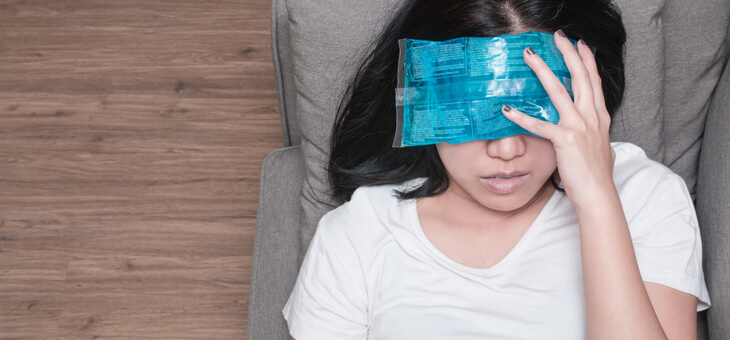 woman lying on couch with ice pack over eyes