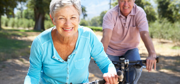 happy older couple riding bikes in park