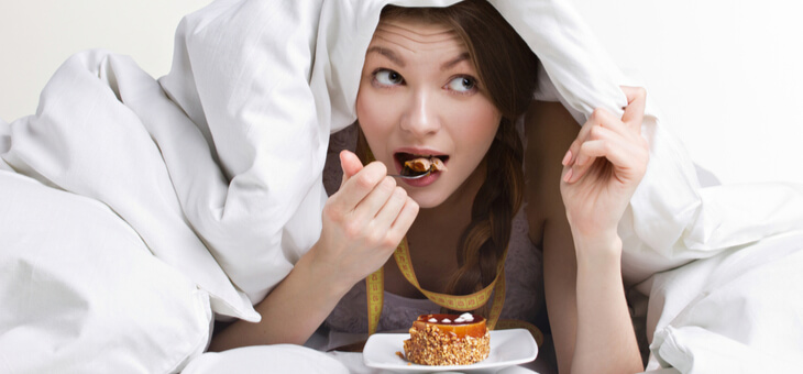 woman eating food under blanket on bed