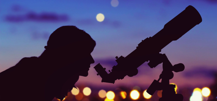 Woman looking through a telescope at night