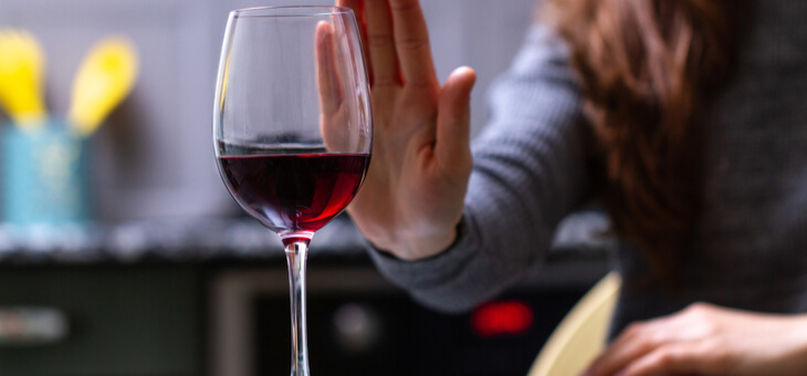 woman holding hand up to refuse glass of red wine