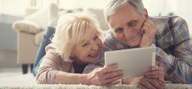 smiling older couple lying on living room floor looking at ipad