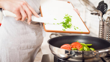 person sliding chopped vegetables from chopping board to pan