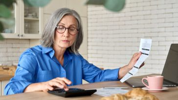 mature woman sitting at kitchen table paying bills on laptop