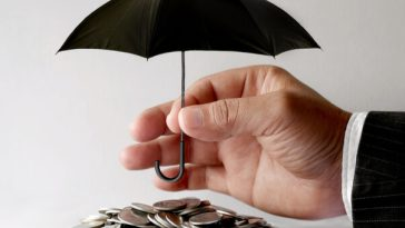man's hand holding tiny umbrella above pile of coins