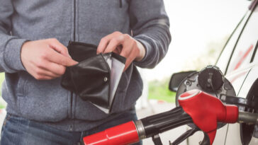 man looking in wallet while filling car with petrol