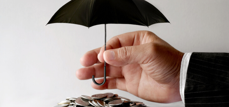 man's hand holding tiny umbrella above pile of coins