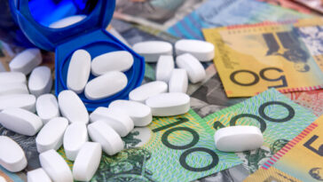white pills spilling from blue bottle on to pile of australian cash