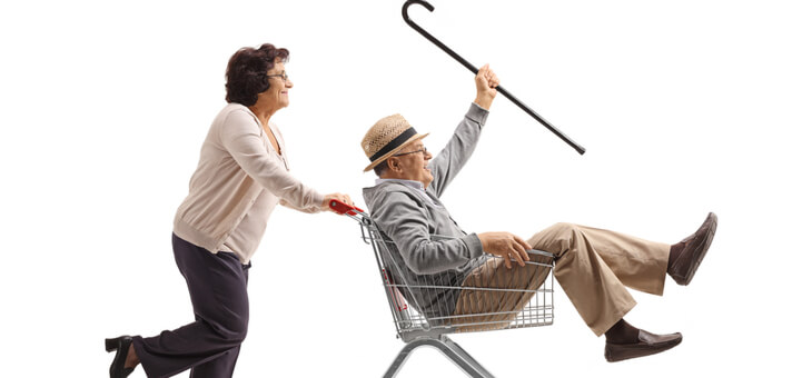 elderly woman pushing elderly man in shopping cart