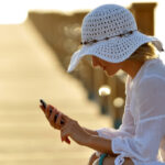 woman sitting on pier using phone at sunset