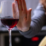 woman holding hand up to refuse glass of red wine